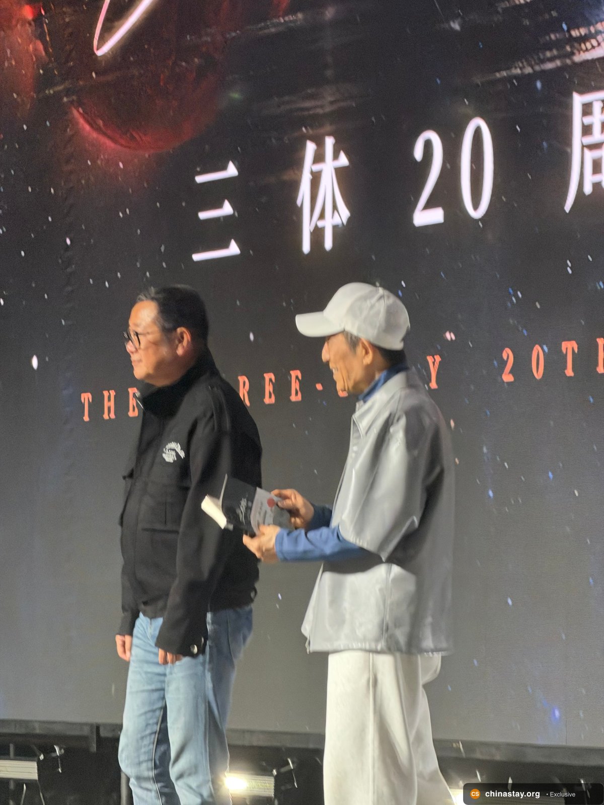 Zhang Yimou holding the autographed Three-Body book on stage with Cixin Liu on Three-Body Day in Beijing